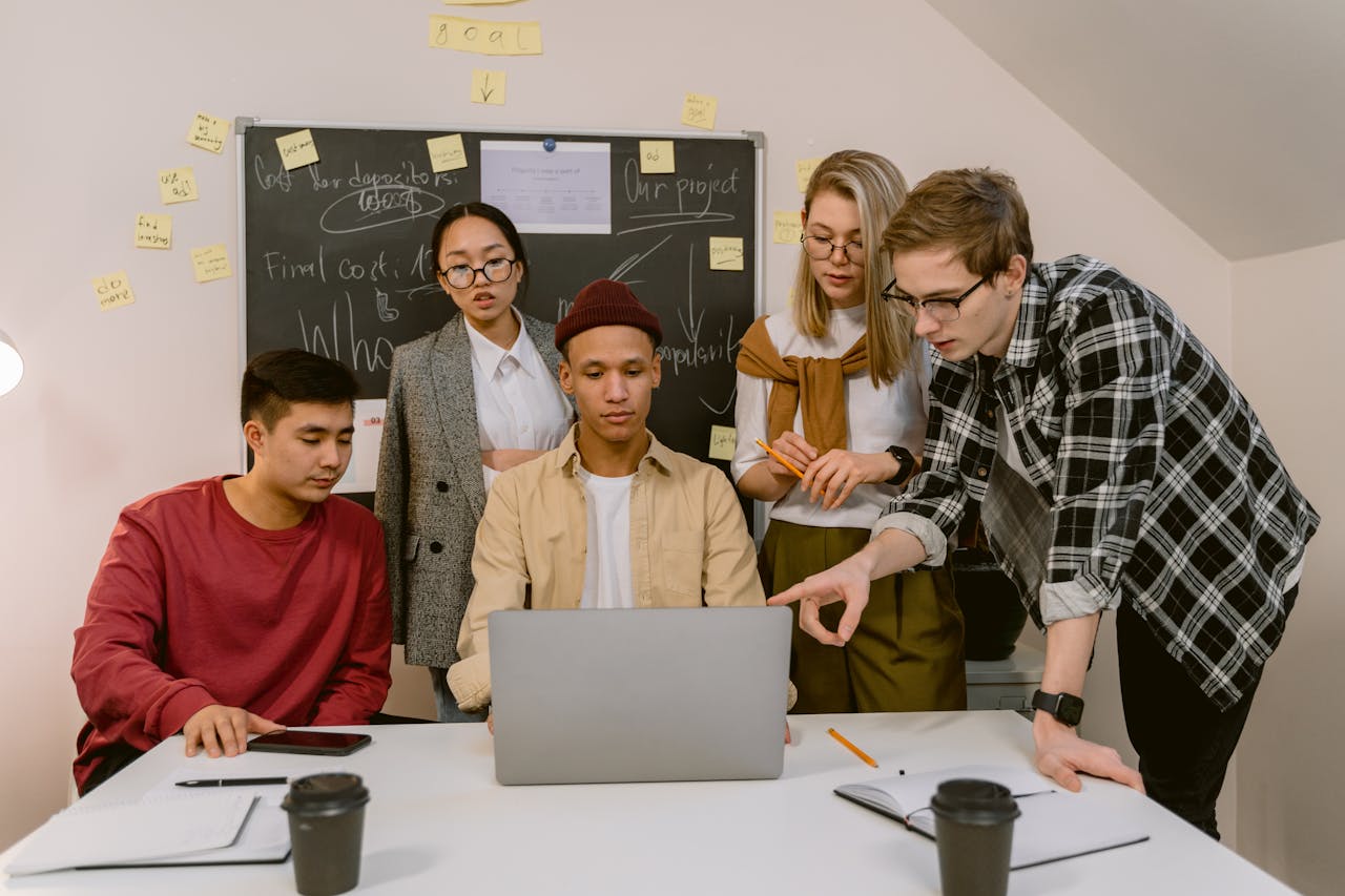 A diverse group of colleagues engaging in a collaborative office meeting with a laptop.